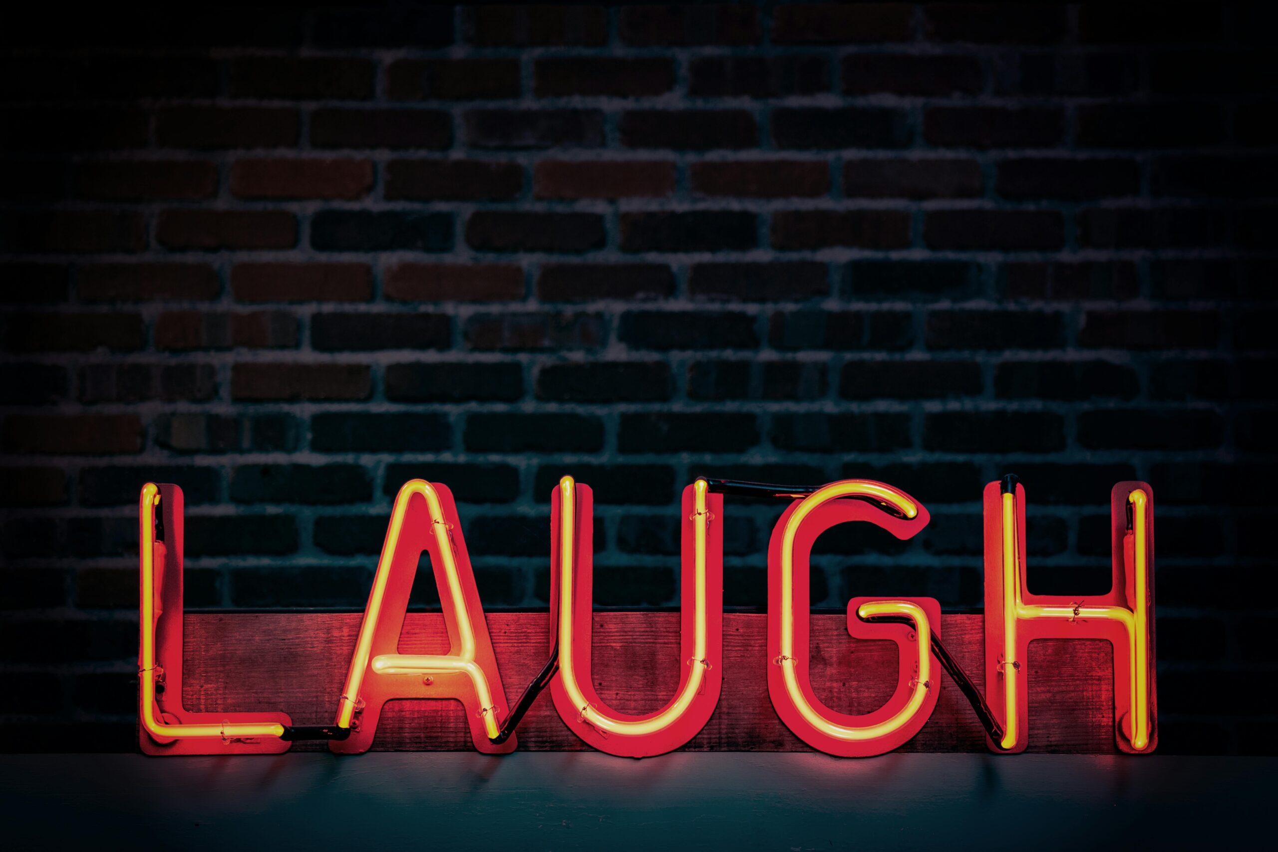 Bright neon sign displaying 'LAUGH' against a dark brick wall, creating a vibrant mood.